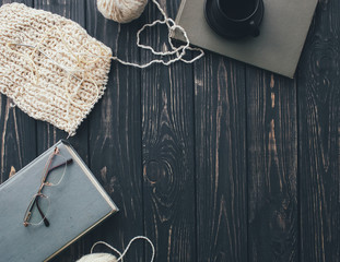 Knitted white sweater , needles , ball of yarn  coffee cup,glasses and book on   white wooden background 