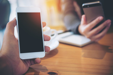 Mockup image of businessman and businesswoman's hands holding and using smartphone on wooden table