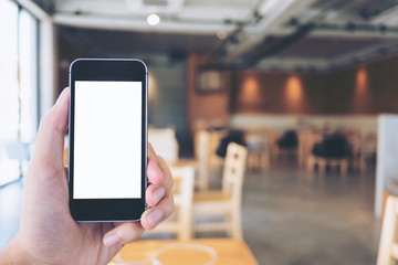 Mockup image of hand holding black mobile phone with blank white screen in modern cafe