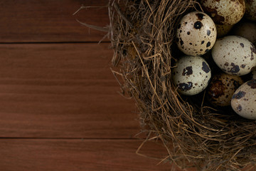 Obraz premium Quail easter egg in nest on wooden table background with copy space, top view. Easter food concept.