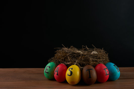 Easter, holidays, tradition and object concept - of colored easter eggs and quaill eggs in nest on wooden surface.black background.Copy space.