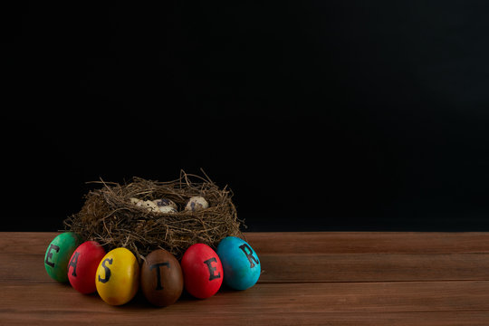 Easter, holidays, tradition and object concept - of colored easter eggs and quaill eggs in nest on wooden surface.black background.Copy space.