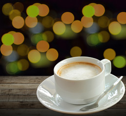 Hot coffee in white cup over wooden background with blurry night light 
