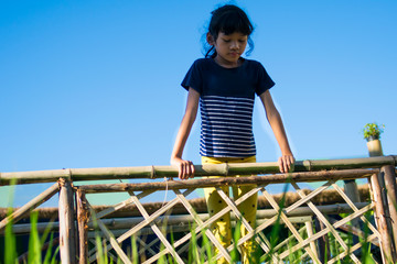 sad little girl standing on bamboo bridge