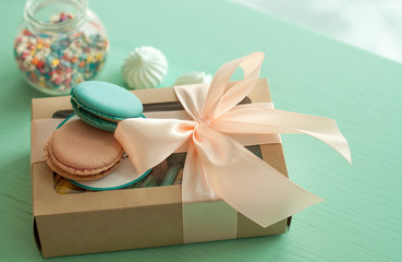 macaroon dessert and a gift in a box for the holiday. On wood, turquoise background