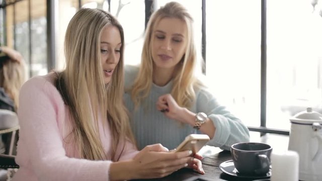 Two women friends speaking in a cafe and looking in smartphone