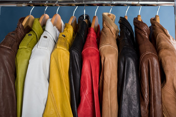 Different color leather jacket hanging on rack on blue background