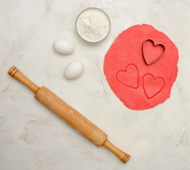 Red dough with a cut out heart, eggs, flour and rolling pin,on a white table. Top view, space for text