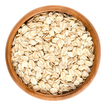 Oatmeal, rolled oats in wooden bowl. Dehusked, hulled oats, rolled into large whole flakes. Porridge oats, used in granola or muesli. Isolated macro food photo close up from above on white background.