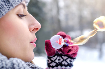 Young beautiful woman blowing bubbles  in winter clothing outdoors.  Focus on lips. Soup bubbles.
