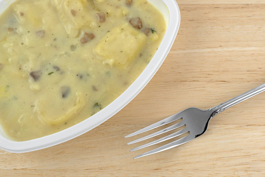 Top close view of ravioli in a cheese and mushroom sauce TV dinner on a wood table with a fork to the side.