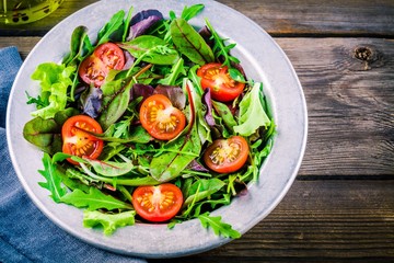 Fresh salad with mixed greens and cherry tomato on wooden background