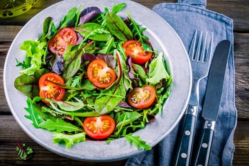 Fresh salad with mixed greens and cherry tomato on wooden background