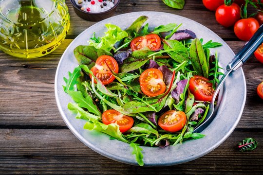 Fresh salad with mixed greens and cherry tomato on wooden background