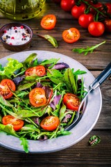 Fresh salad with mixed greens and cherry tomato on wooden background