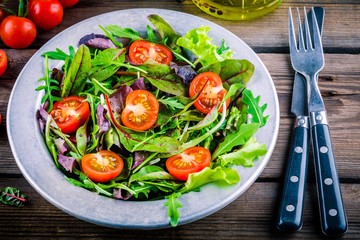 Fresh salad with mixed greens and cherry tomato on wooden background