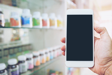 Hand holding mobile smart phone with blank screen for text on blurred pharmacy background, concept of drugstore and business pharmacy.