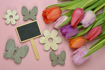 Wooden pink background with fresh colorful spring tulips and empty copy space blackboard tag label and  butterfly and flower decoration made of wood.