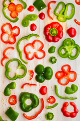 Food styling image design of red and green bell pepper slices on white wooden cutting board.