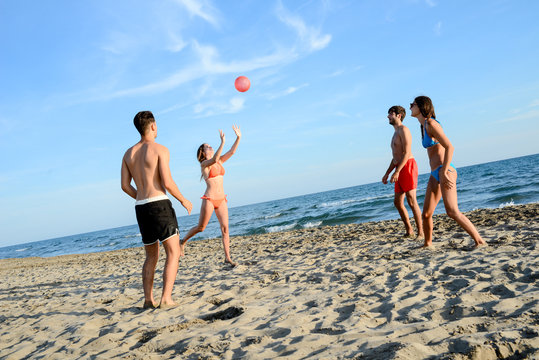 Four Young People Man And Woman Playing Beach Volley Together By The Sea In Sunny Summer Vacation Day