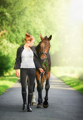 Tierliebe - junge, hübsche Reiterin führt Pferd am Halfter in der Frühlingssonne