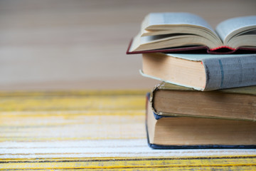 Open book, stack of hardback books on wooden table.