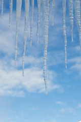 Closeup of icicles against a blue sky with clouds