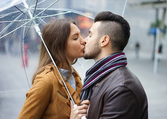 Beautiful young couple having tender moments on a rainy day standing under a transparent umbrella...