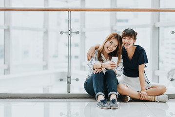 Obraz premium Young happy Asian girls best friends laugh and smile while having fun with smart phone mobile indoor.