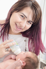 Modern young mother giving milk to her baby from bottle