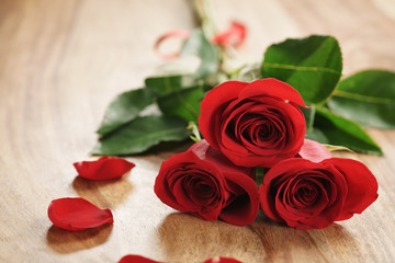 three red roses and petals on old wood table closeup, romantic background