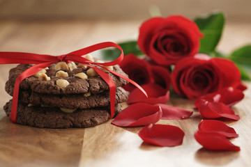 three red roses with homemade chocolate cookies on old wood table closeup, romantic background