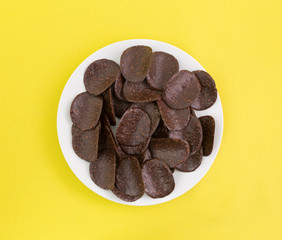 Chocolate covered rice crisps on a white plate atop a yellow tablecloth.