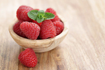 wood bowl full of ripe raspberries with mint leaves on old wooden table, with copy space