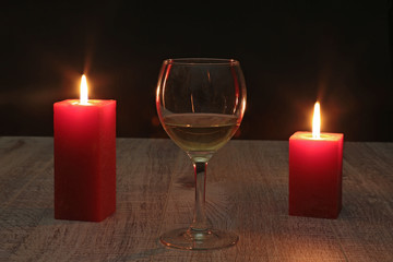 glass of wine or cognac and red candle on a wooden background.