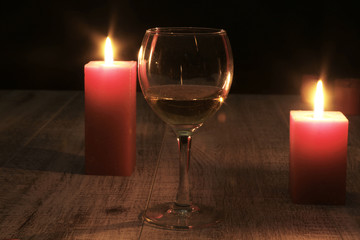 glass of wine or cognac and red candle on a wooden background.