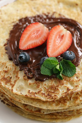fresh blinis or crepes with melted dark chocolate and berries, closeup photo