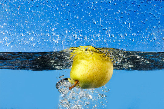 fresh pear dropping into water on blue background