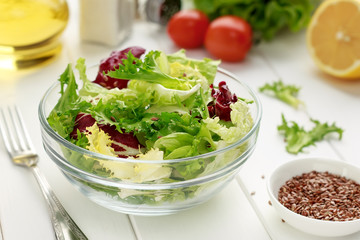 Fresh green salad in bowl with flax seeds, oil, lemon on white wooden table.