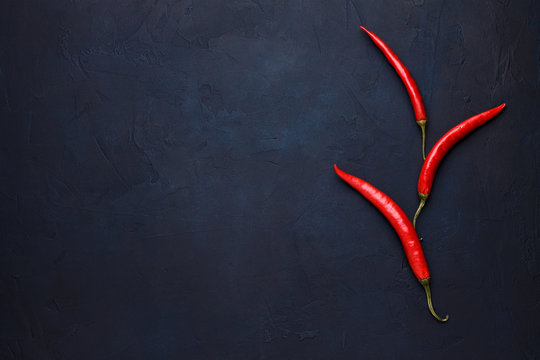 Three red chili peppers on the dark blue stone background.