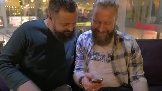 Close up view of two white mature bearded men using smartphone together. Men are relaxing and smiling