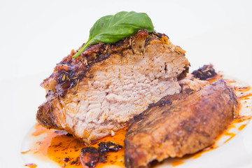 Roast pork decorated with basil on a white plate