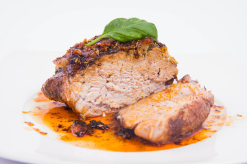 Roast pork decorated with basil on a white plate
