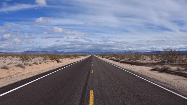 Time lapse clouds floating over two lane desert highway with vanishing perspective on sunny day