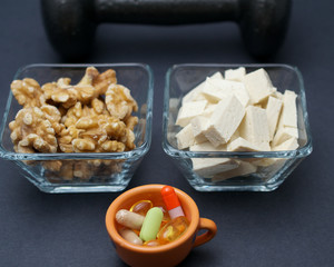 Dumbbells, tofu, nuts and dietary supplement on black background- muscle building on a vegan diet