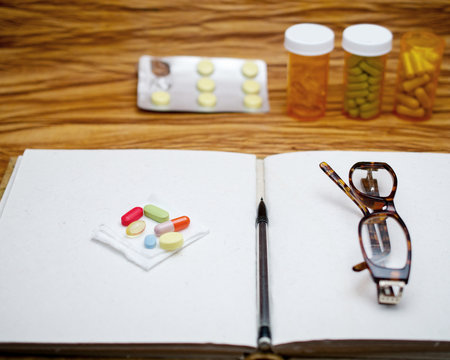 Open blank journal, pair of readers and medicine tablets suggesting the concept of memory loss