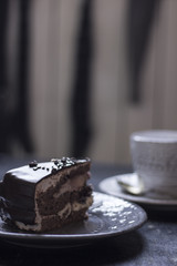 A cup of coffee together with a delicious slice of a chocolate cake on a white and dark worn out background.
