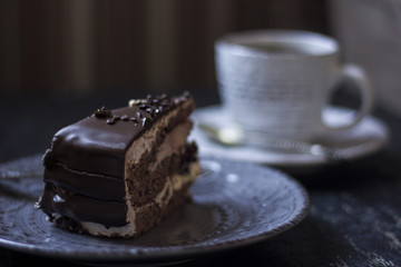 A cup of coffee together with a delicious slice of a chocolate cake on a white and dark worn out background.