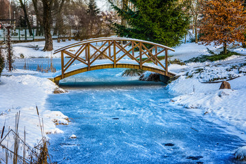 Winter in the park. Snowy, wooden bridge over frozen pond. Poland.