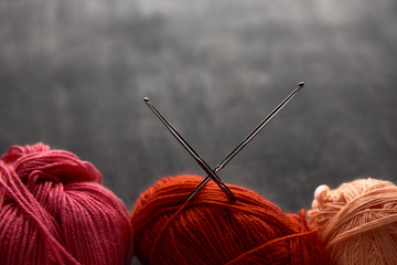 Red, rose and orange balls of yarn on wooden background with soft focus.